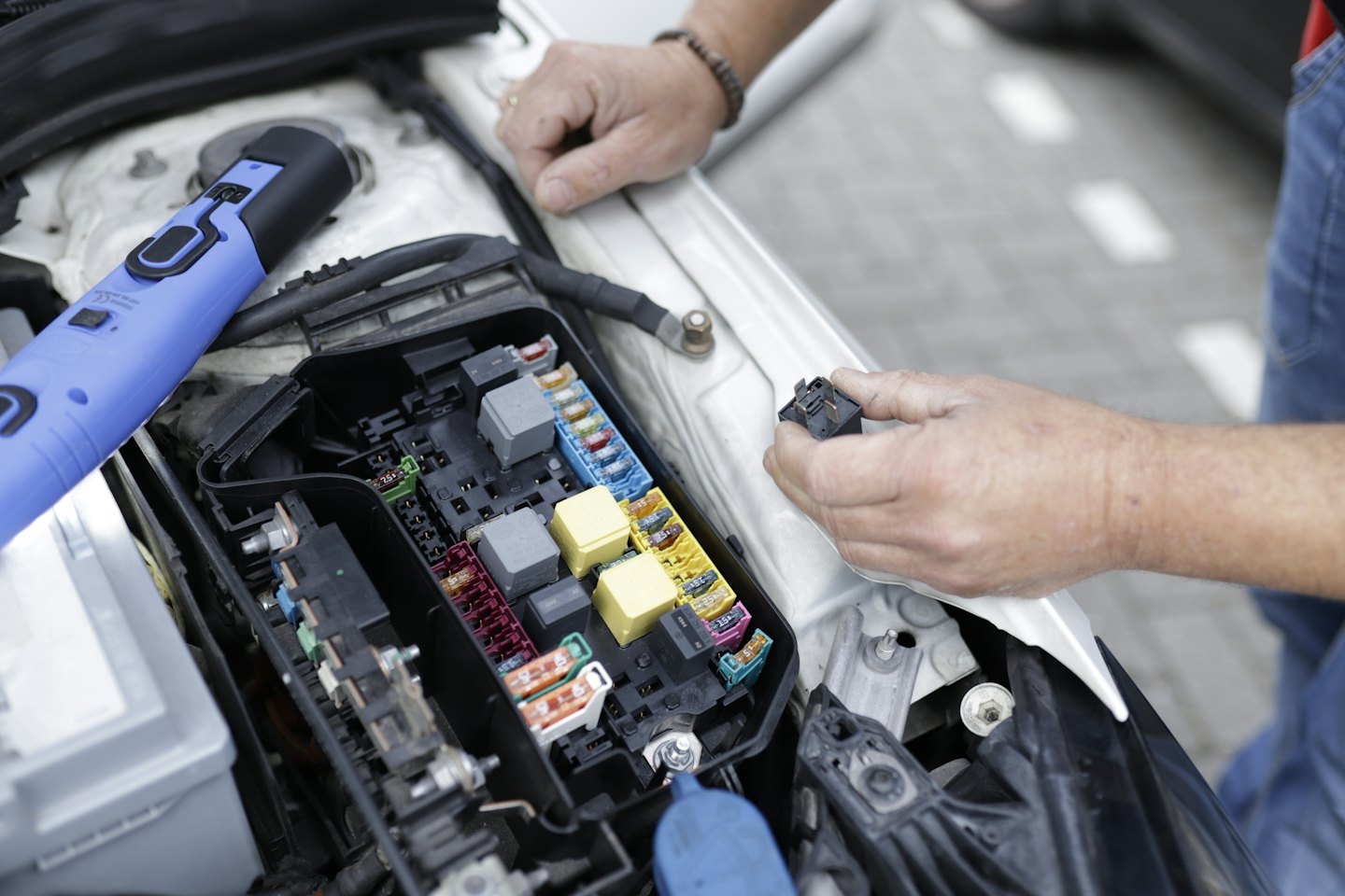 Mechanic's hands inspecting a car's fuse box and electrical components.