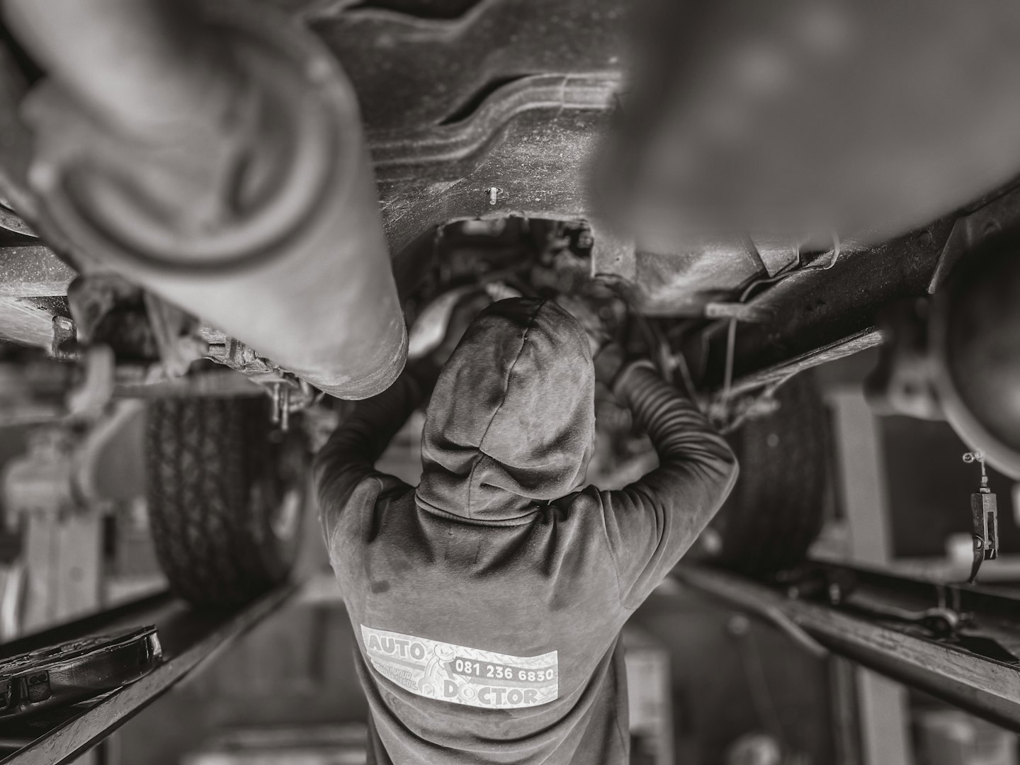 Mechanic working on car underside in a garage.