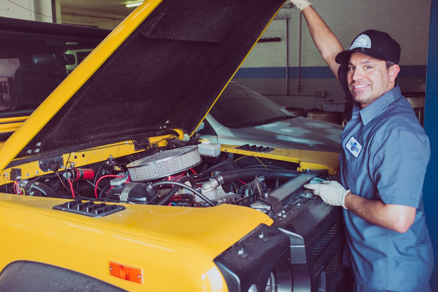 Smiling mechanic in blue uniform with yellow car.